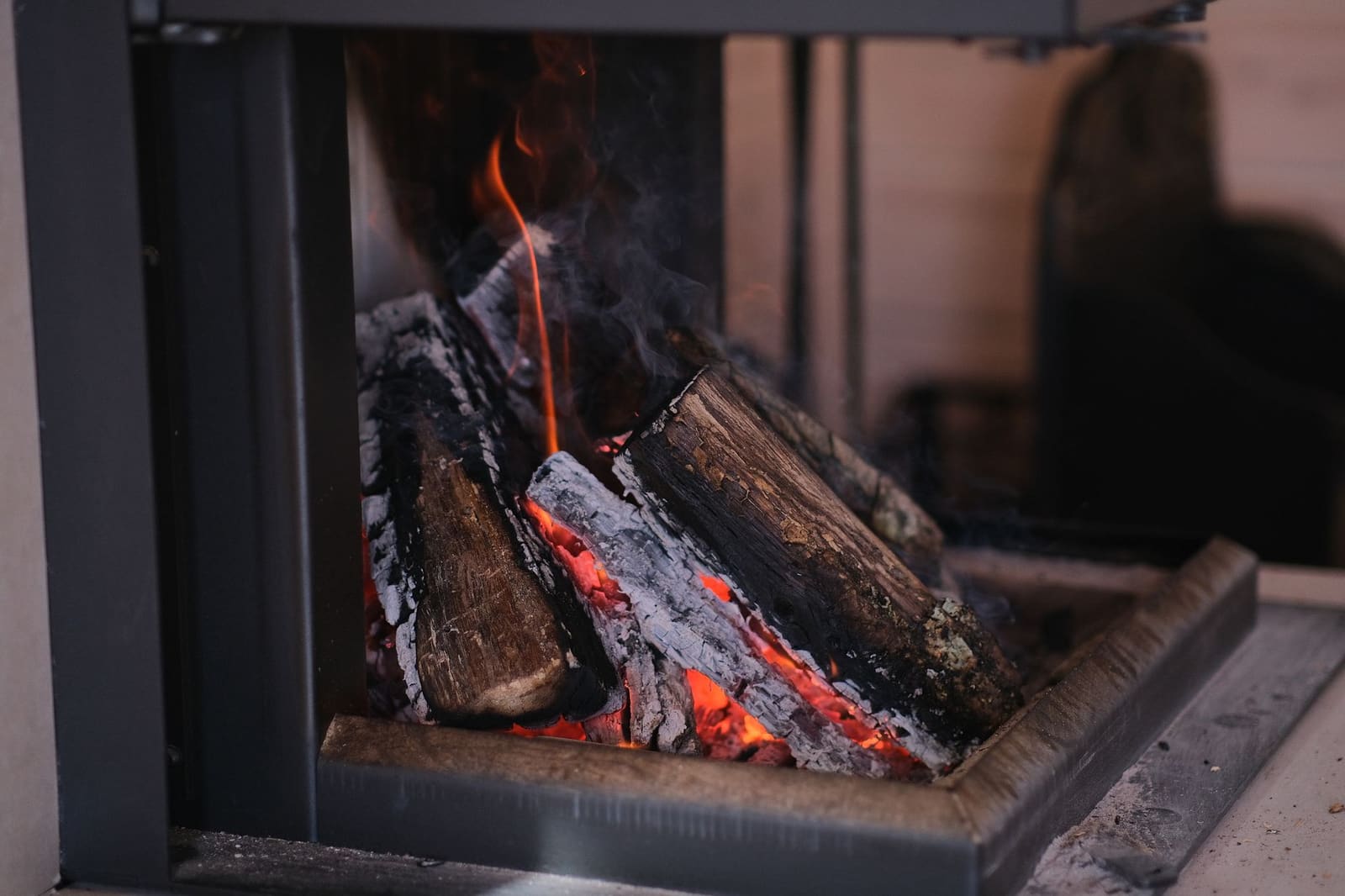 Split logs burning in a steel-framed firebox with ash on the hearth