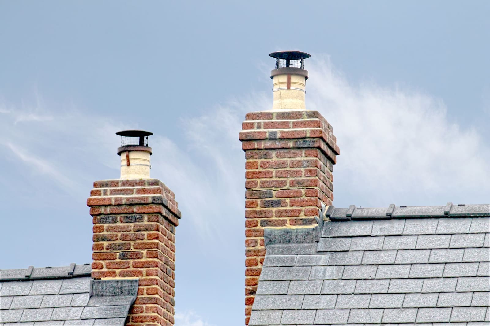 Two brick chimneys with round metal caps and mesh screens fitted over clay flue pots